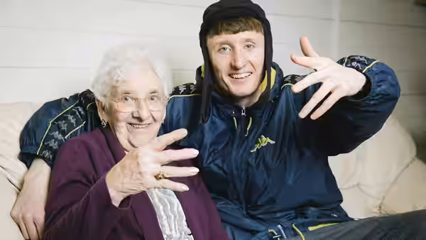young man and elderly woman sit on a couch making hand gestures