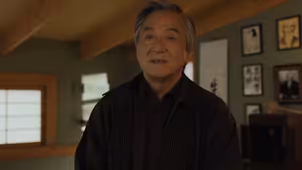 Mr. Han (Jackie Chan) stands in a room lined with framed photographs