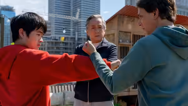 Li Fong practices a punch as Mr. Han watches and another man raises his arm