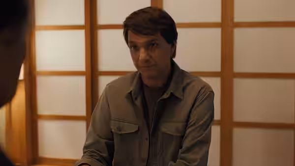 A man sits before shoji screens, facing someone just outside the frame