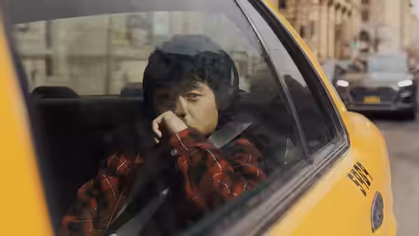 Li Fong rides in a yellow taxi, holding a hand near his mouth