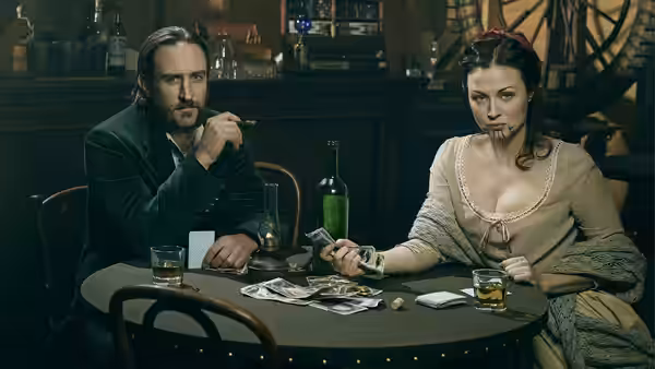 Cullen Bohannan and Eva sit across a table with drinks and cards