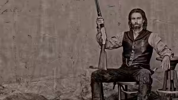 Cullen Bohannan sits holding a rifle against a plain backdrop