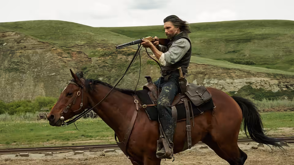 Cullen Bohannan (Anson Mount) rides a horse across open grassland, holding a rifle
