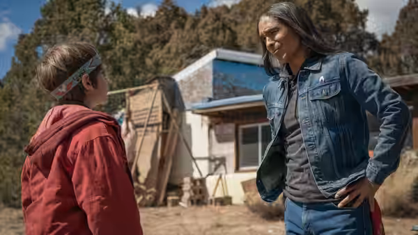 A long-haired man talks with a young person outside a trailer