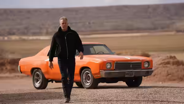 Dillon Macintosh (Eric Dane) walks past an orange car on a roadside
