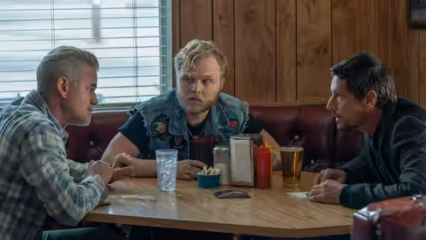 Lefty Ledbetter (Paul Walter Hauser) sits between two men in a diner booth