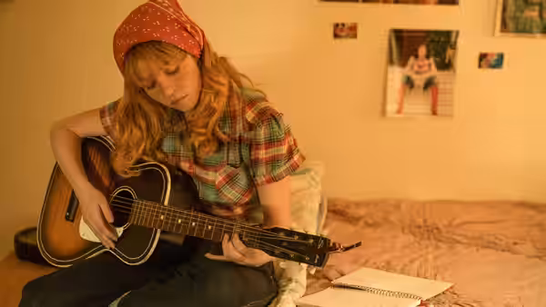 Penny Jo Poplin (Sydney Sweeney) plays guitar in a room