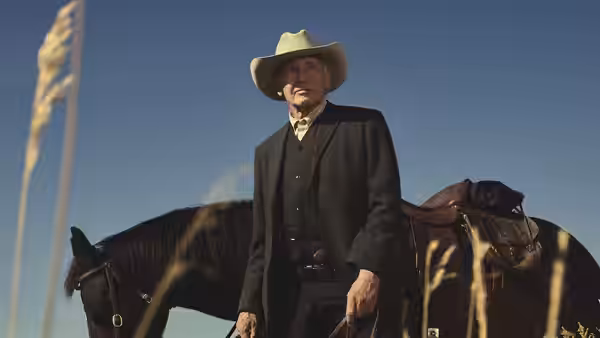 Jacob Dutton (Harrison Ford) stands beside a saddled horse in tall grass