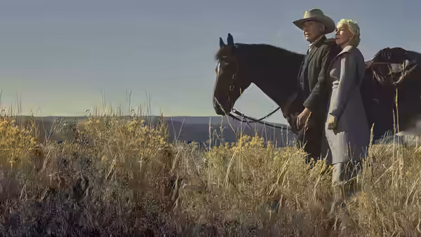 Jacob Dutton (Harrison Ford) and Cara Dutton (Helen Mirren) stand beside horses in a grassy field