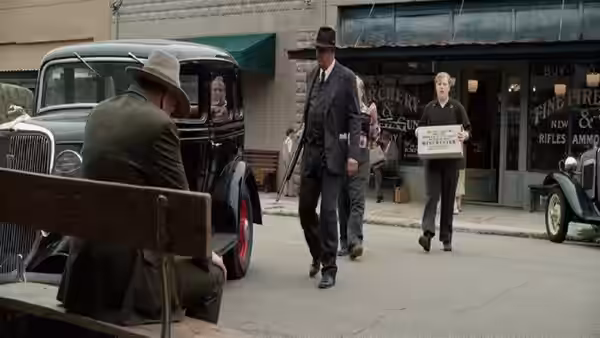 Frank Hamer (Kevin Costner) walks past a seated man outside storefronts