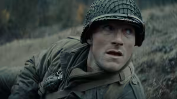 A helmeted soldier in a netted steel helmet looks upward against a concrete wall