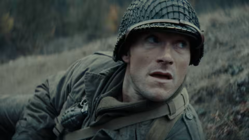 A helmeted soldier in a netted steel helmet looks upward against a concrete wall