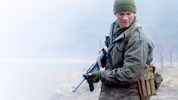 A soldier in a wool cap holds a rifle beside an open field