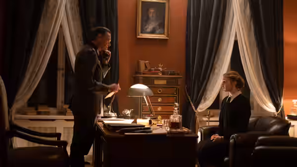 A uniformed man speaks with Irena Gut Opdyke (Sophie Nélisse) across a desk in an office