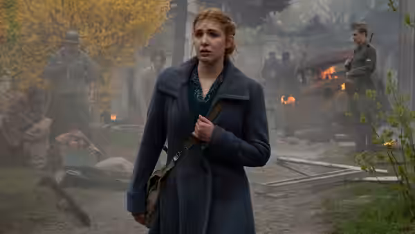 Irena Gut Opdyke (Sophie Nélisse) stands in a misty outdoor cemetery as figures work behind her