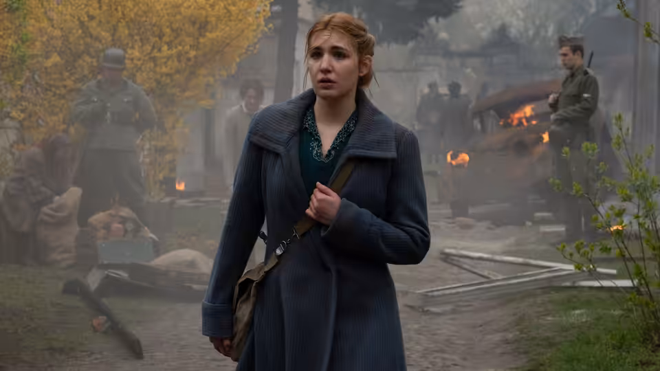 Irena Gut Opdyke (Sophie Nélisse) stands in a misty outdoor cemetery as figures work behind her