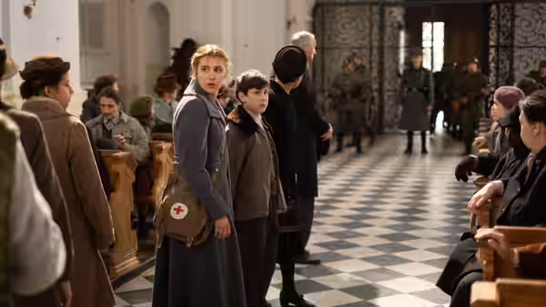 Irena Gut Opdyke (Sophie Nélisse) stands among people seated in a checkered-floor hall