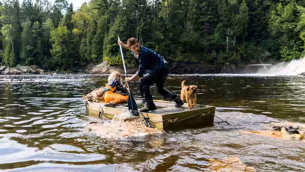 Todd Hewitt (Tom Holland) stands aboard a small boat beside a seated passenger and a dog