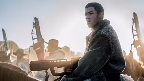 Todd Hewitt (Tom Holland) holds a rifle amid a dusty settlement
