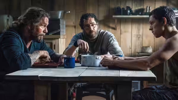 Todd Hewitt (Tom Holland), Ben Moore (Demián Bichir), and Cillian Boyd (Kurt Sutter) gather around a pot in the kitchen