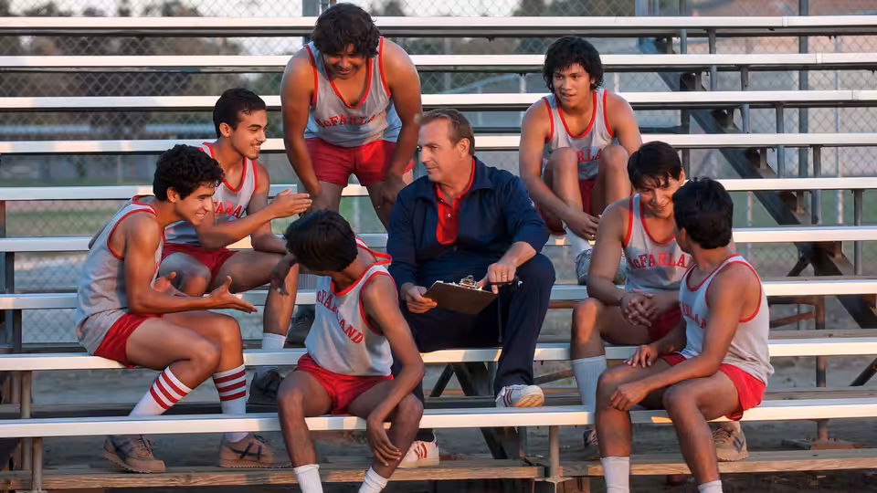 Jim White (Kevin Costner) reviews a clipboard with McFarland runners seated around him