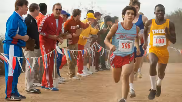 Runners sprint past spectators and coaches at a cross-country race