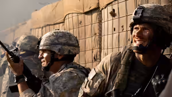 Two soldiers take cover beside a fortified wall, one aiming his rifle