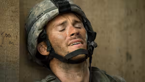 A helmeted soldier rests against a wall with his eyes closed