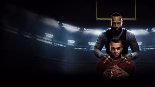 Isaiah places his hands on Cam's shoulders in a dimly lit stadium