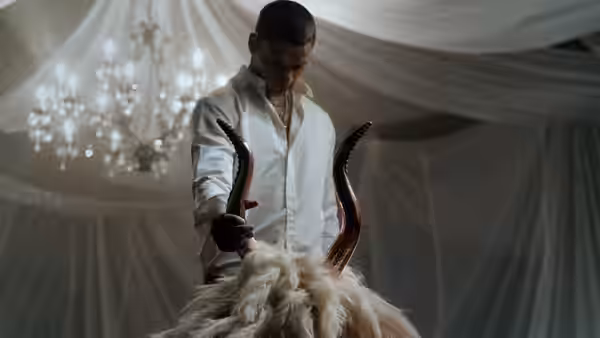 Cam holds a horned animal skull beneath a chandelier in a draped room