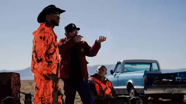 Isaiah (Marlon Wayans) gestures beside Cam in orange sportswear near a parked pickup truck