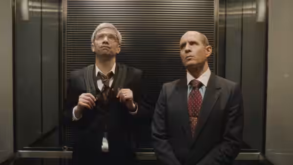 Jim (Glenn Howerton) stands beside a bespectacled man inside an elevator