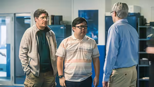 Three men discuss work among computer monitors in an office