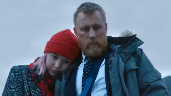 A bearded man stands with a girl leaning against him in the snow
