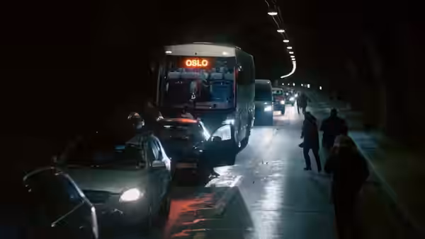 Cars and a bus marked Oslo queue inside a tunnel as people walk past