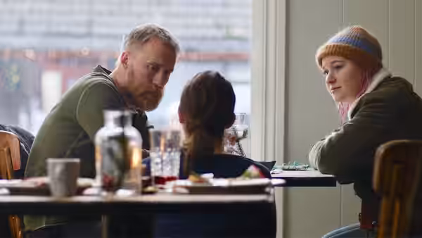 A bearded man sits at a table with two young women in a café