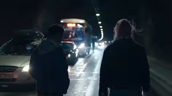 Two people stand among stopped cars and a bus inside a dim tunnel