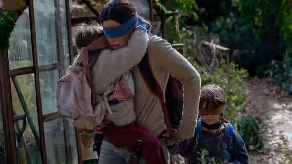 Blindfolded Malorie (Sandra Bullock) carries a baby as a boy follows behind