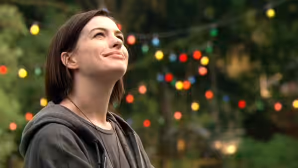 Kym (Anne Hathaway) smiling upwards at an outdoor evening gathering with lights