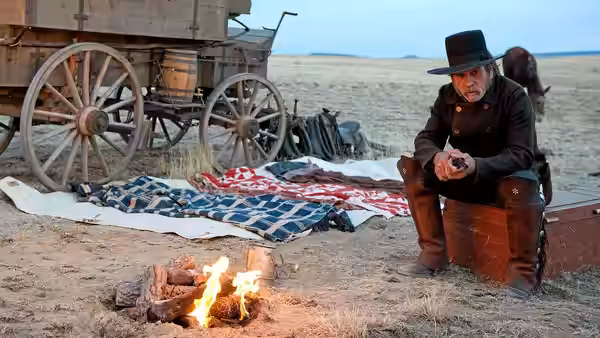 George Briggs (Tommy Lee Jones) sits beside a campfire near a covered wagon