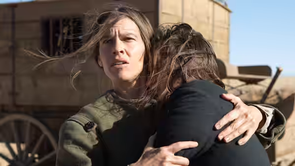 A woman embraces another woman beside a wagon, looking anxiously toward the distance