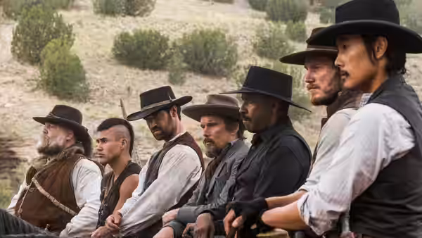 Seven armed men sit in a row on horseback in the open country