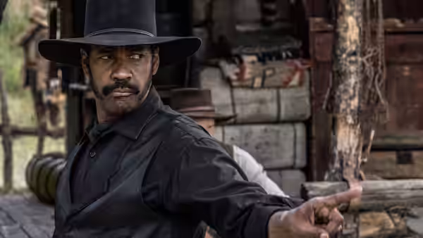 Sam Chisolm (Denzel Washington) points toward someone outside a wooden storefront