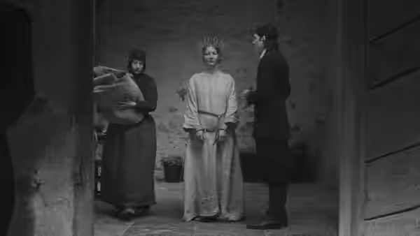 A woman stands with bound hands between two men in a bare room