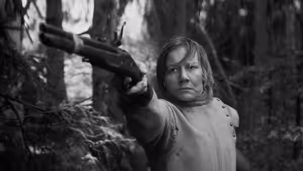 A short-haired woman aims a rifle among the trees