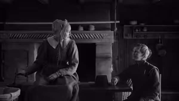 Two women face each other across a table in a farmhouse kitchen