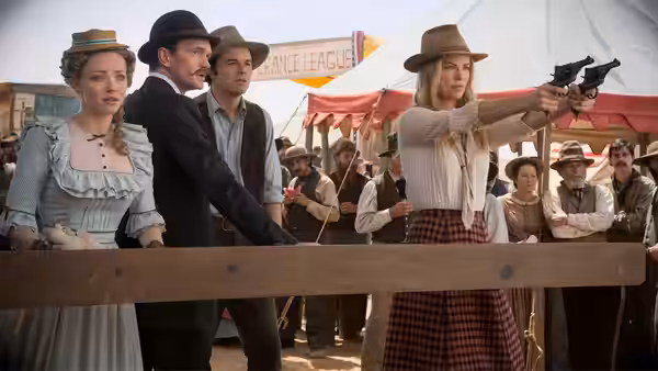Anna aims a revolver over a wooden rail as townspeople watch
