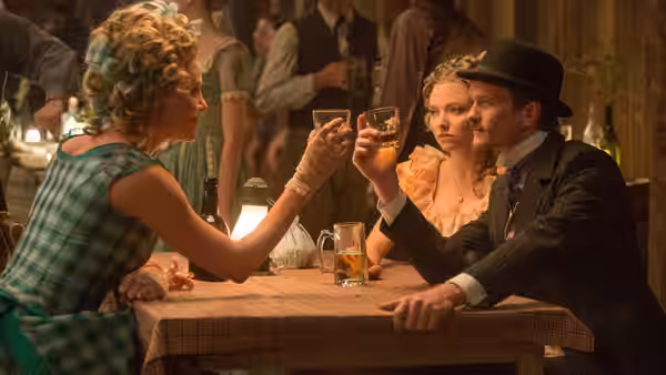 Ruth and Albert raise glasses across a table while Louise looks on