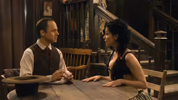 Albert and Anna sit facing each other across a wooden table indoors
